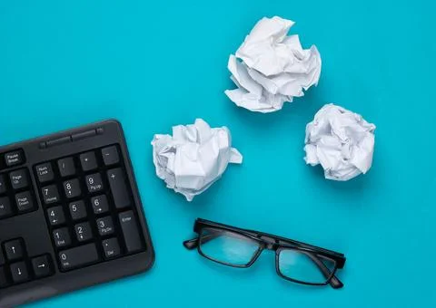 Office flat lay. PC keyboard, crumpled paper balls, glasses on a blue studio  Stock Photos