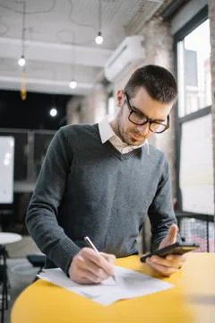 Office guy using phone and writing on paper Stock Photos