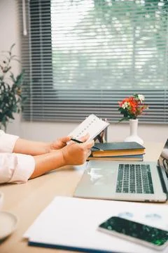 Office professional writing notes beside laptop, books, phone, and flower o.. Photos