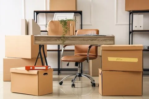 Office relocation and moving boxes with desk and chair, business transition a Stock Photos
