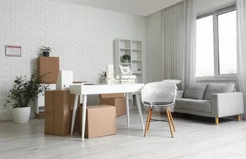 Office relocation and moving boxes in a bright modern workspace with desk and Stock Photos