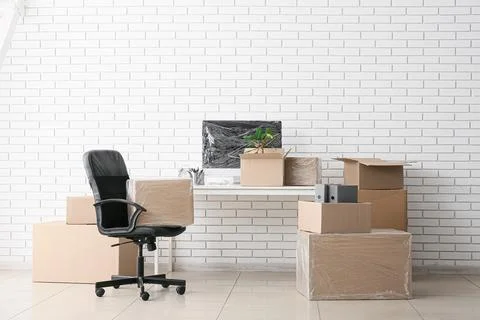 Office relocation and moving day with packed cardboard boxes, desk, and chair Stock Photos