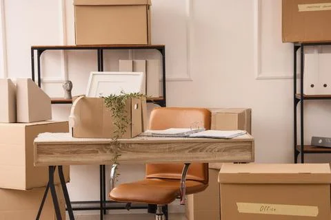 Office relocation and moving day logistics with cardboard boxes, desk, and ch Stock Photos