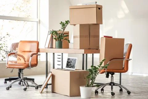 Office relocation with cardboard boxes, desk, and chairs in a bright, empty r Stock Photos