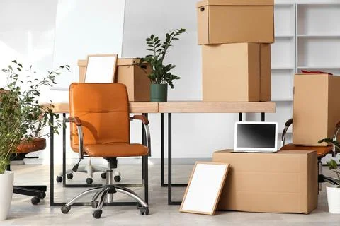 Office relocation with cardboard boxes, desk, and chairs for business moving  Stock Photos