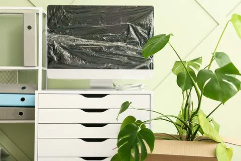 Office relocation with a desktop computer wrapped in plastic and a monstera p Stock Photos