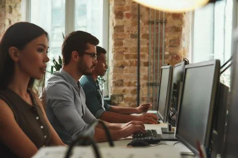 Office routine. Side view of young employees working on computers while sitting Stockfoto's