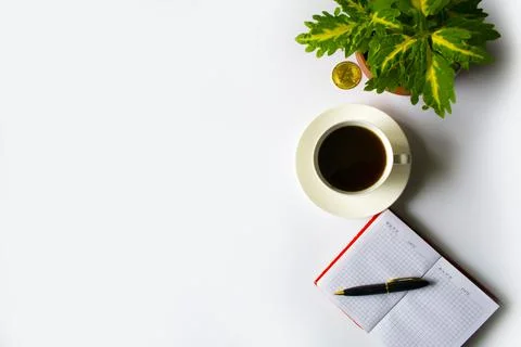An office table with a cup of coffee, next to a notebook in a red note. Nearby Stock Photos