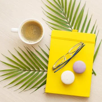 Office table with yellow notepad, cup of coffee, glasses, macaroons on palm Stock Photos