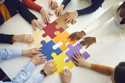 Office team assembling jigsaw puzzle pieces on table top view on hands Stock Photos