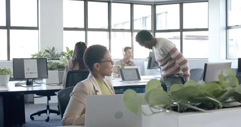 Office team reviewing work after man turning chair and approaching seated woman Stock Footage 345589354