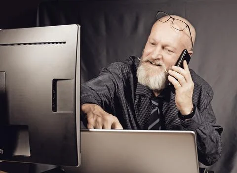 Office work - cheerful elderly man with a gray beard talking on the phone in Stock Photos