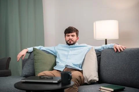 An office worker with a beard sat down on a sofa with pillows to take a nap Stock Photos