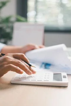 Office worker calculating financial data with calculator while reviewing bu.. Stock Photos