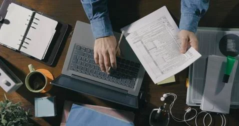 Office worker checking paperwork and using a laptop Stock Photos