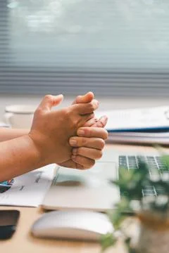 Office worker clasping hands above laptop and financial report at desk, sho.. Stock Photos