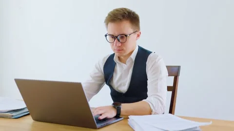 An office worker, dressed in a suit and glasses, types away on his laptop in a Stock Footage 236632492