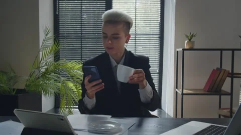 Office worker drinks her coffee when texting message indoors. Business lady Stock Footage 253631300