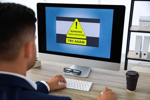 Office worker in front of computer with warning about virus attack on screen Stock Photos