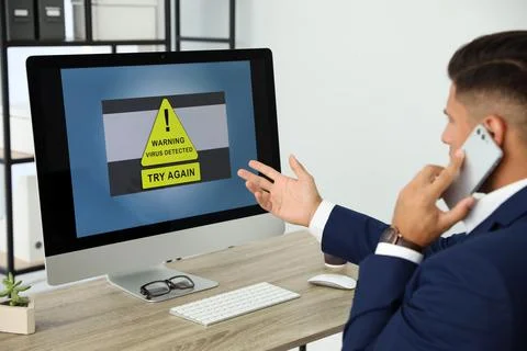 Office worker in front of computer with warning about virus attack on screen Stock Photos