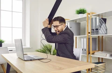 Office worker gets angry at computer because of error and wants to smash it with Stock Photos