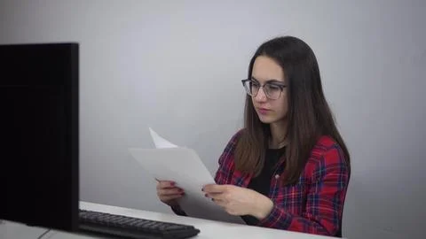 Office worker looks at documents at the workplace in the office. Young woman in Stock Photos