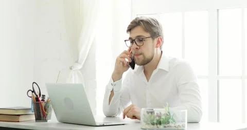 Office worker man is talking on smartphone looking on document at laptop screen. Vídeo Stock 132101266