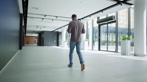 Office worker with phone walking down lobby 스톡 동영상 112050912