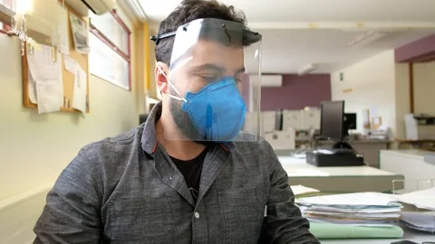 Office worker with plastic protective screen and face mask working on compute Stock Footage 129392259