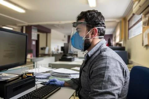 Office worker with plastic protective screen and face mask working on compute Stock Photos