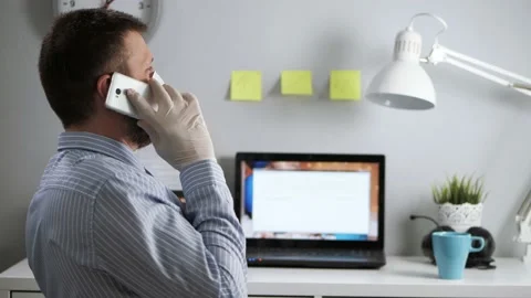 Office worker in protective mask is talking on phone. Bearded man in surgical Видео 130310942