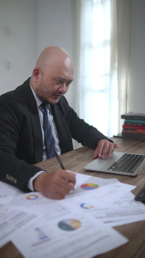 Office Worker Reviewing Financial Reports and Taking Notes While Using a Laptop Stock Footage 336870487