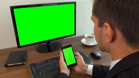 An office worker sits at a desk and looks at a computer and a smartphone with Stock Footage 103452665