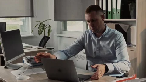 Office worker sits down at a desk with a compact laptop gets to work Stock Footage 307597685