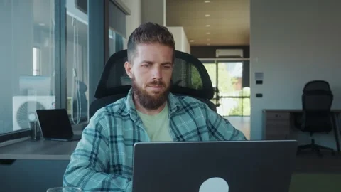 Office worker sitting at desk, looking away in thought while using laptop Stock Footage 312120638