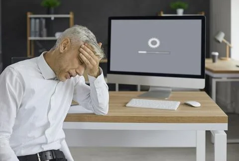 Office worker sitting in front of desktop computer and waiting for system to Foto stock