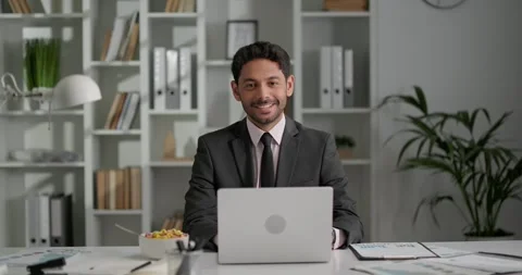 Office worker sitting at his workplace, working on laptop, looking at camera. Stock Footage 248965967