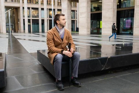 Office worker sitting on stone bench outdoor holding umbrella while waiting Foto stock