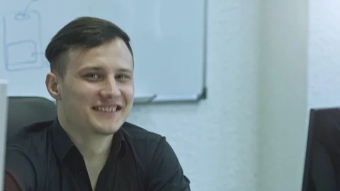 Office worker smiling and looking at camera. Attractive young man using computer Stock Footage 105809185