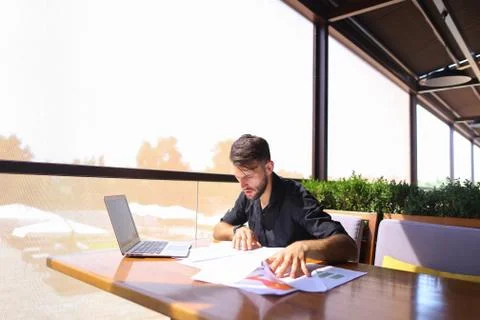 Office worker sorting papers on table near laptop. Stock Photos