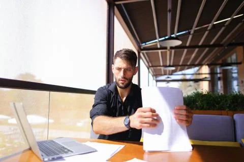 Office worker sorting papers on table near laptop. Stock Photos