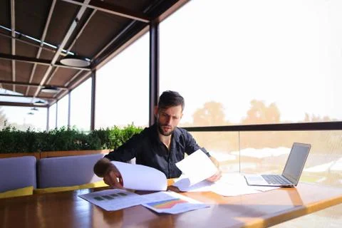 Office worker sorting papers on table near laptop. Stock Photos