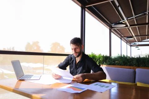 Office worker sorting papers on table near laptop. Stock Photos