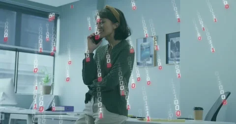 Office worker speaking on smartphone at desk, binary digits rising around her Stock Footage 321435134