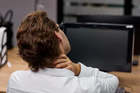 Office worker stretching neck while seated at desk with computer during workday Stock Photos