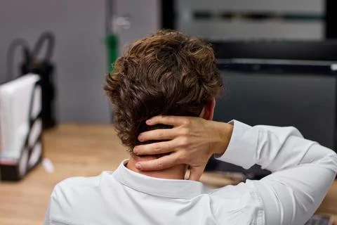 Office worker stretching neck while seated at desk with computer during workday Stock Photos