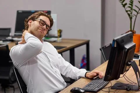 Office worker stretching neck while seated at desk with computer during workday Stock Photos