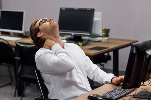 Office worker stretching neck while seated at desk with computer during workday Stock Photos