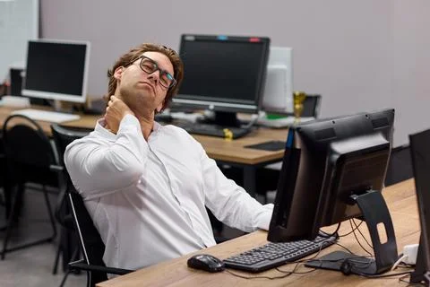 Office worker stretching neck while seated at desk with computer during workday Stock Photos