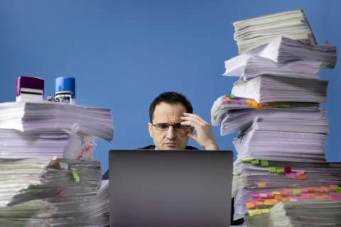 Office worker swamped with documents doing overtime project on laptop computer Stock Photos